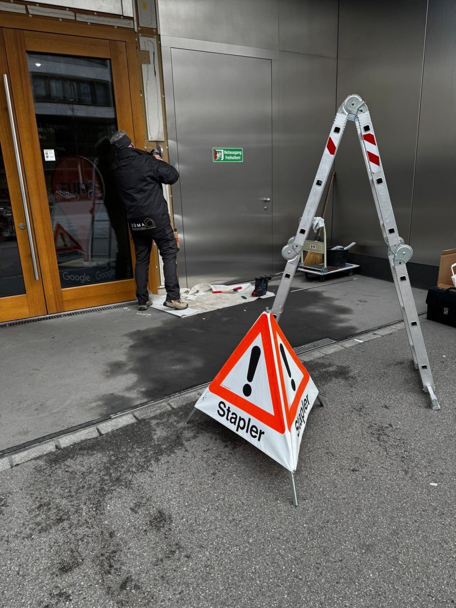 Arbeiter reinigt Eingang; Warnschild und Leiter vor Ort