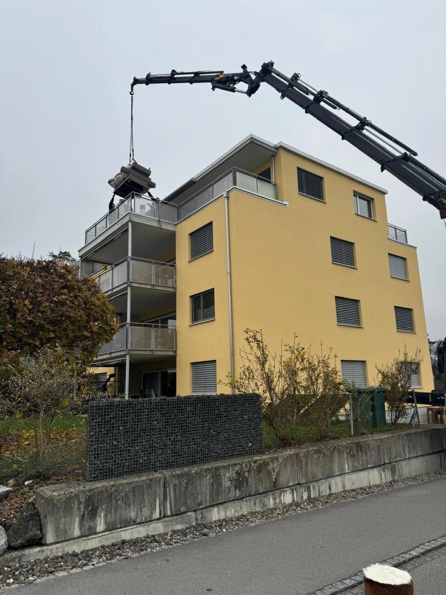 Kran hebt Material auf Dach eines gelben Wohnhauses